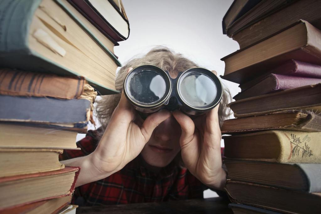 man using binoculars in between stack of books